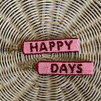 two sided pink keychains with 'Happy + Days' text on a each beaded surface